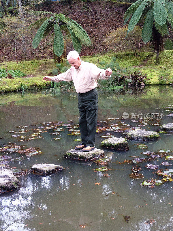 在葡萄牙亚速尔群岛圣米格尔岛的Terra Nostra植物园，一位老人在池塘中行走，展示平衡和活力。